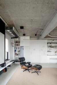 Open living area with white walls and floors, featuring a black chair, couch, and bookshelves in a modern space with a bright and inviting atmosphere
