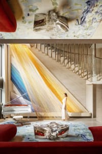 Interior space with a staircase, wooden railing, piano, and natural light from windows, with two women present