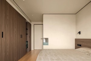 Empty minimalist bedroom with a large white wall, wooden floor, and two doors leading to other areas of the house