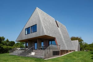 A modern house with a triangular shape and wooden exterior, featuring several windows that allow natural light to enter the interior spaces