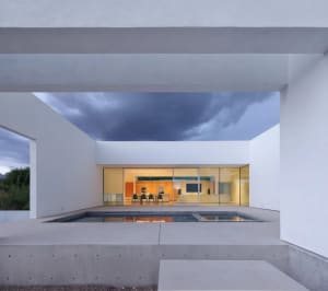 Open modern living area with a white wall, chairs, a dining table, and clean lines