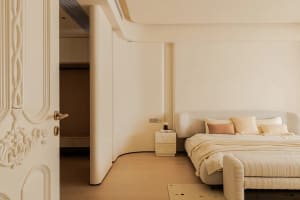 Empty minimalist bedroom with a white bed against a wall, hardwood floor, and white walls