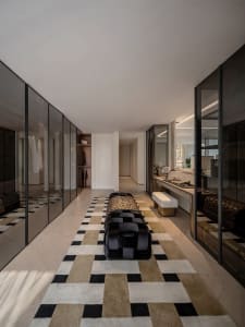 Open modern living area with a black couch, white walls and floors, two chairs, a potted plant, and a glass wall