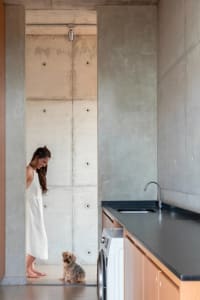 A woman stands in a kitchen with a sink, oven, and refrigerator, surrounded by casual, lived-in decor