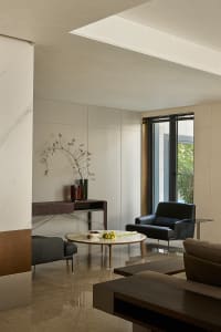 Modern living room with a black leather couch, a chair, a dining table, and a potted plant, set against a backdrop of white walls and wooden floors