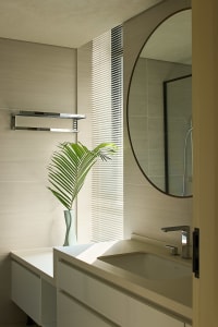 Bathroom with white tiles, a sink, mirror, and shower area, featuring two potted plants and a large mirror above the sink