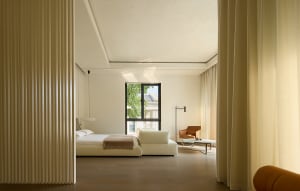 Open living area with a white couch near a window, a chair, and a dining table in a modern and minimalistic space with clean lines and neutral tones