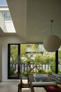 A modern dining space with a round light fixture, two dining tables, a potted plant, and a chair, set in a well-lit atmosphere