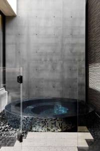 A modern bathroom with a large, round, blue-tiled bathtub and stone tub, situated next to a wall in a modern and elegant space