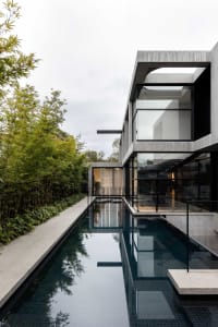 A modern house with a swimming pool in its backyard, surrounded by a fence, and featuring large windows for natural light
