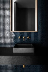 Bathroom with a sink, mirror, and black tile wall, set against a blue tile floor, creating a modern and clean atmosphere