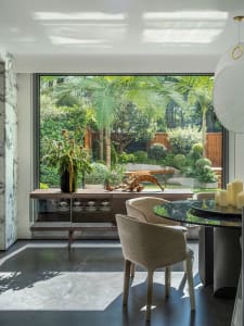 A living area with a large window, two chairs, a dining table, and decorative elements, flooded with natural light