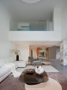 Open living space with a white couch, smaller couch, chairs, dining table, potted plants, and decorative vases in a clean and minimalist style with neutral tones