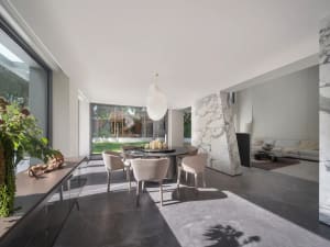 Open modern living space with a dining table, chairs, and a couch near a large window allowing natural light to fill the space