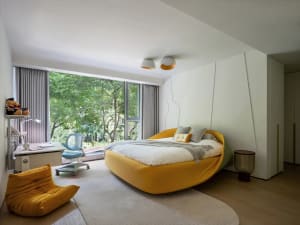 A bright and inviting bedroom with a large yellow bed, two chairs, and a window allowing natural light to enter