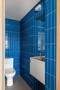 Bathroom with blue tiles, a white toilet, and two sinks, one with a cupboard underneath, in a modern and clean design