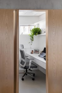 A cozy office space with a desk, two chairs, a laptop, and a potted plant, set against a neutral background