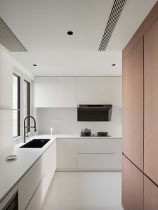 A modern kitchen with white cabinets, countertops, and two sinks, featuring a black oven and a clean design