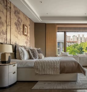 A modern bedroom with a large white bed, hardwood floor, and artwork on the walls, filled with natural light from two windows