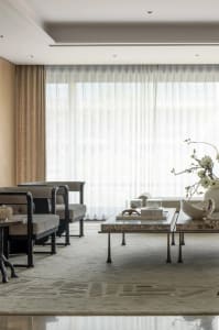 Warm and inviting living room with three couches, two chairs, and two dining tables, surrounded by white curtains
