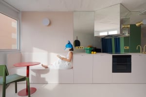 Woman reading a book in a cozy kitchen with white cabinets, a dining table, and fresh fruit on the countertop