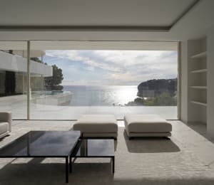 Open living area with two white couches in front of large windows offering ocean views, surrounded by modern home design with clean lines and minimal decoration