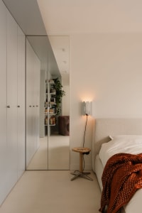 A cozy bedroom with a white bed, red blanket, nightstands, a mirror, and a potted plant