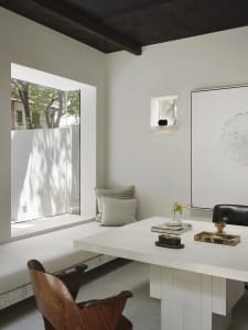 Open living area with a white table, chairs, couch, and a potted plant, surrounded by natural light and bright atmosphere