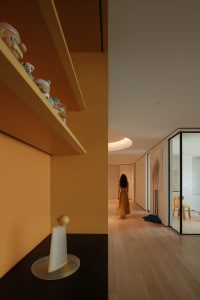 A woman walks down a hallway with a wooden floor, vases, and chairs, creating a warm and inviting atmosphere