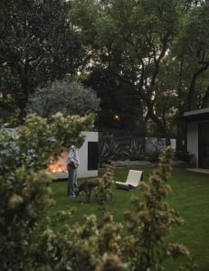 A relaxed outdoor living area with a fire pit, two chairs, and a bench, set amidst a natural landscape
