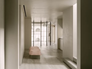 A white room with a pink bench and two chairs, featuring a large window for natural light