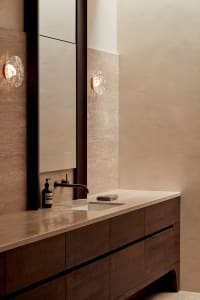 Modern bathroom with a brown countertop, sink, and mirror, with two bottles on the counter, in a well-lit space
