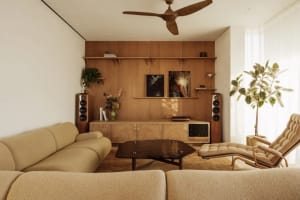 Open living area with wooden floors and walls, featuring a seating arrangement, coffee table, and natural light from a large window