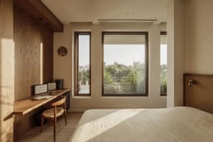 Bright and inviting bedroom with a wooden floor, a chair near the window, clocks, and a book on a surface