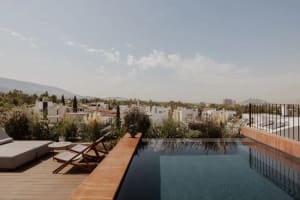 A rooftop pool area with two chairs, surrounded by trees and city buildings, creating a relaxing atmosphere