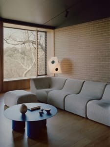 A modern living room with a large couch, two chairs, a dining table, and a vase, featuring a clean and minimalist design with neutral tones and a focus on functionality
