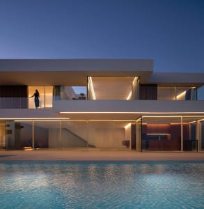 A modern white house with glass walls, a swimming pool, and a spacious living area with a couch and dining table