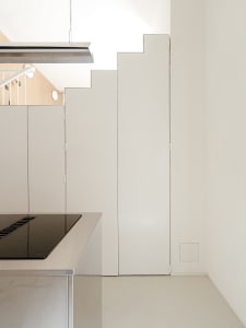 Modern kitchen with white walls and cabinets, featuring a stove top oven, refrigerator, and two sinks, with a focus on functionality and clean lines