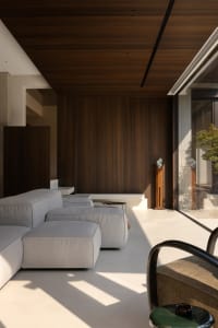 A modern living area with a couch, chairs, and bench, surrounded by wooden walls, natural light, and a dining table, creating a warm and inviting atmosphere