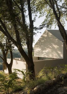 A house with a white exterior, surrounded by trees, featuring a large window and two smaller windows