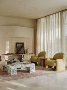 A warm and inviting living area with a large window, two chairs, a dining table, and decorative vase, surrounded by natural light