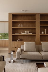 A well-lit living room with two couches, three chairs, and two bookshelves, featuring a warm and elegant wooden theme