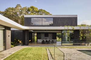 Open modern living area with a large kitchen, dining table, and living room, featuring white walls, black accents, and natural light from several windows