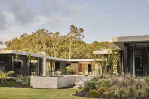 A modern house with a large glass wall facade, surrounded by two potted plants and three outdoor chairs, set in a contemporary and stylish living environment