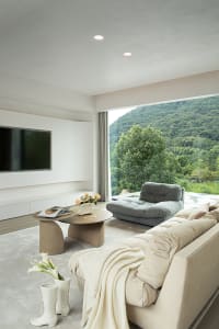 Cozy living room with a modern design, white walls, wooden floors, a large couch, a chair, and a flat screen TV, with vases placed throughout the space