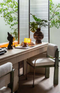 Cozy workspace with a wooden desk, chair, books, plants, and a cup, set against a neutral background