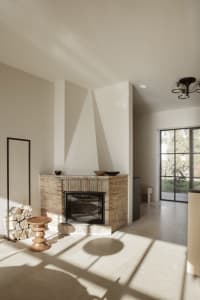Cozy living room with a brick fireplace, a couch, a chair, and a dining table, featuring white walls and warm lighting