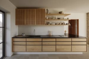 A modern kitchen with wooden cabinets, black countertops, a sink, dining table, and various kitchenware