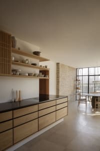 Warm kitchen with wooden cabinets, black countertops, and white walls, featuring a dining table and chairs, and decorative vases and bowls