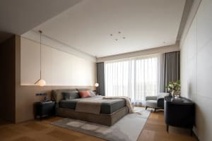 A modern bedroom with a gray bed, two chairs, and a couch, well-lit by natural sunlight